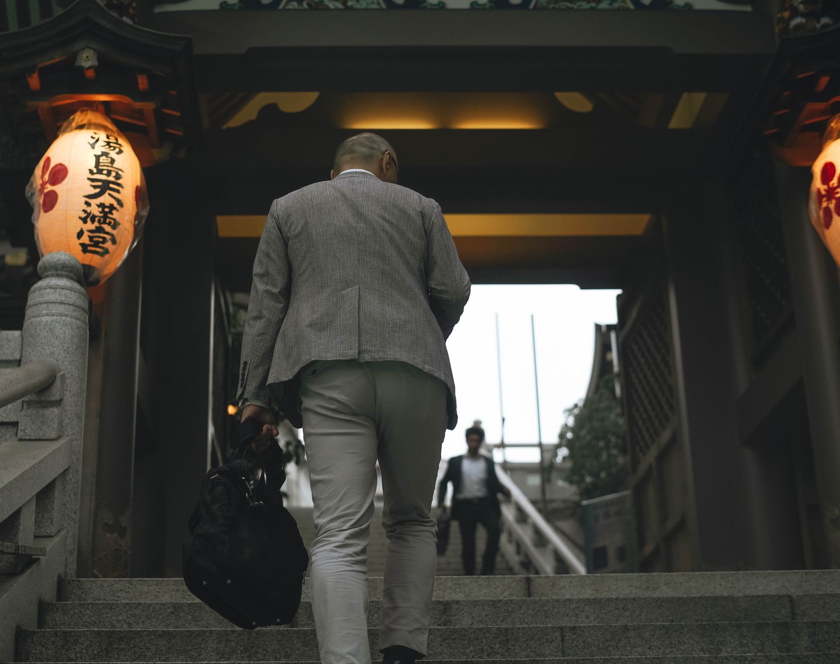 Japanese businessman ascending a staircase in Tokyo, Japan. Captured from behind with lanterns and traditional architect